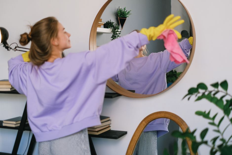Three professional cleaners from Cleaners Hampstead are depicted inside a modern living room, engaged in surface cleaning. The room features a light-colored wooden floor that appears dust-free and wel