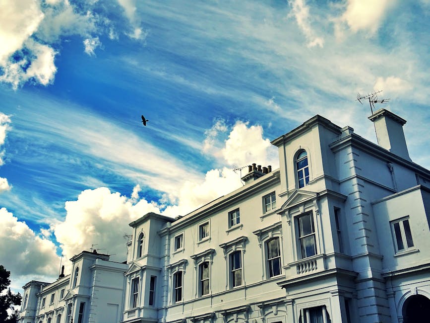 Image of a row of white Victorian-style terraced houses in Hampstead, featuring ornate architectural details, black wrought-iron balconies, and black iron fences along the pavement. The buildings have